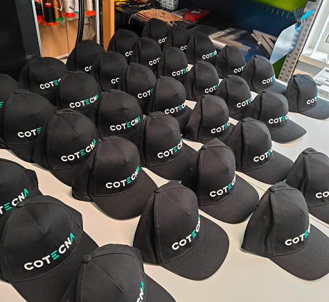 Serie zwarte caps met het geborduurde bedrijfslogo van Cotecna Serie zwarte caps met het geborduurde bedrijfslogo van Cotecna
