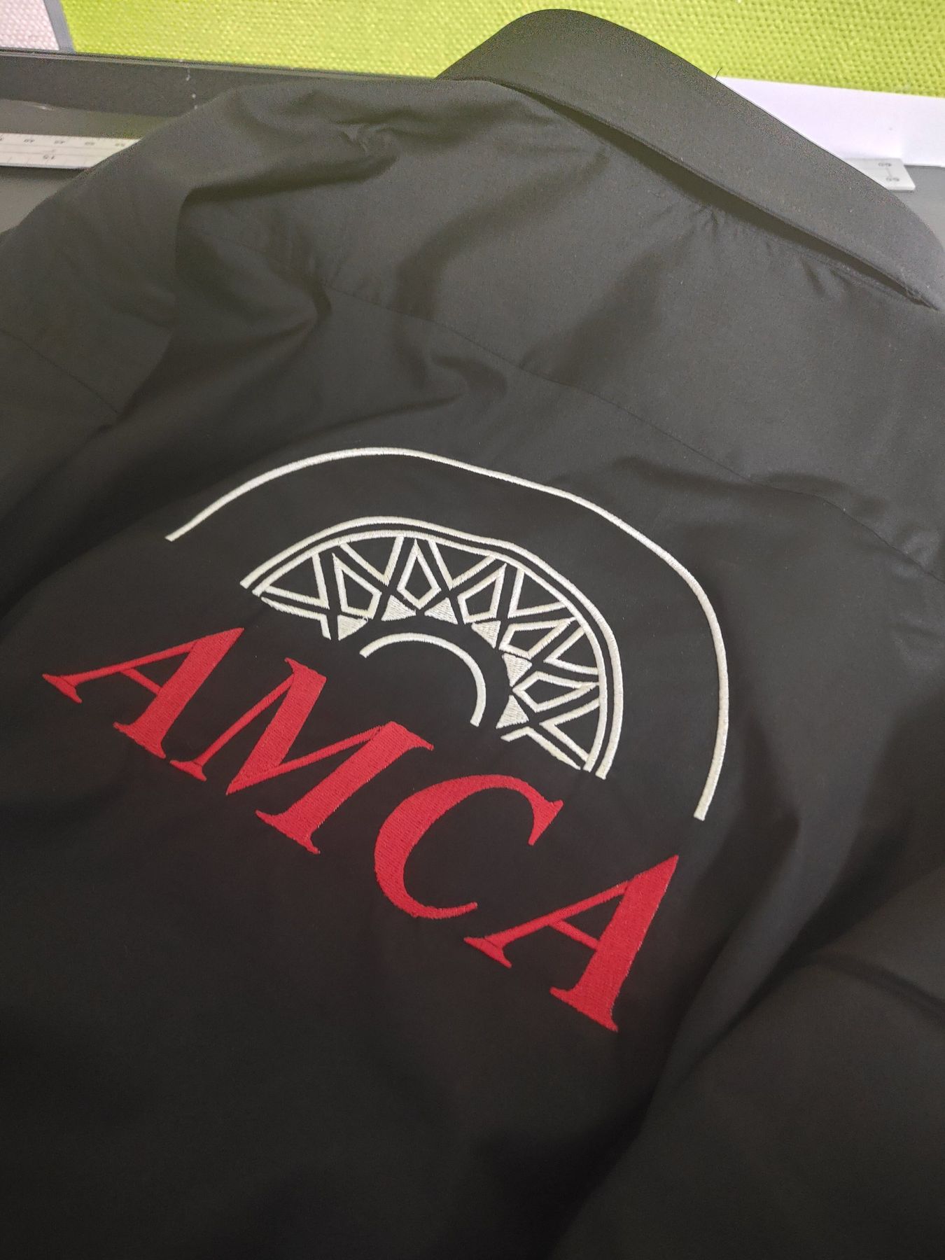 Zwarte jas met een groot geborduurd AMCA-logo in rood en wit